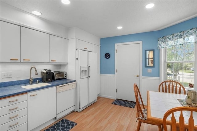 kitchen featuring a sink, light wood-style floors, a wainscoted wall, white cabinetry, and white appliances