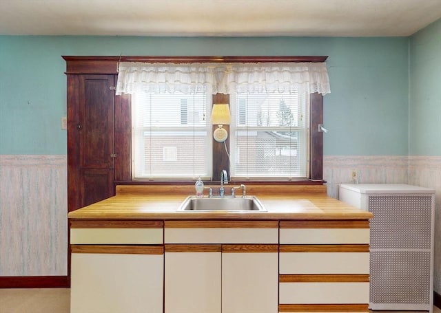 kitchen featuring a wainscoted wall, light countertops, and a sink