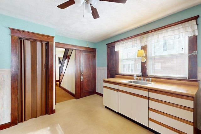 interior space with a wainscoted wall, light floors, light countertops, white cabinetry, and a sink