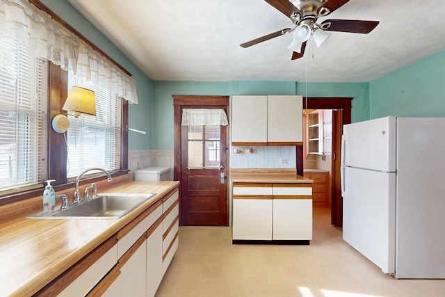 kitchen featuring light countertops, a sink, freestanding refrigerator, and white cabinets