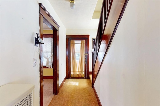 hallway with stairs, baseboards, and light colored carpet