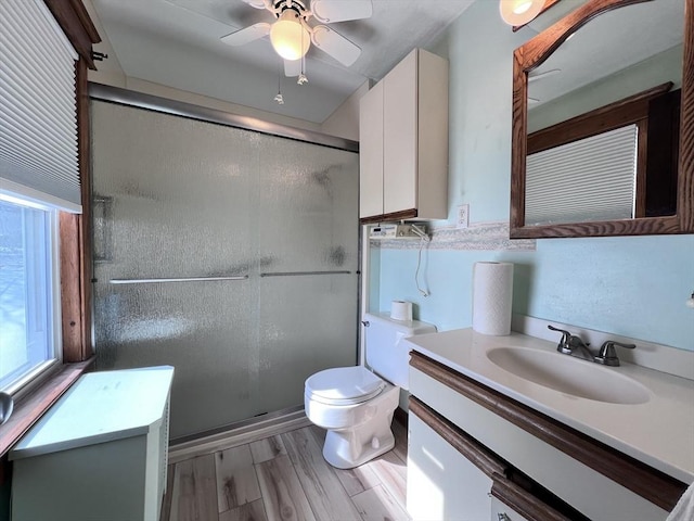 bathroom featuring a stall shower, toilet, ceiling fan, wood finished floors, and vanity