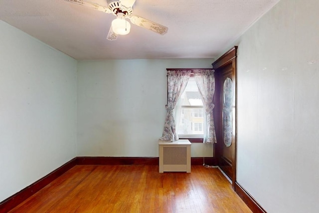 unfurnished room with wood-type flooring, baseboards, ceiling fan, and radiator heating unit