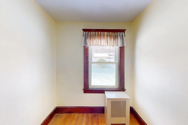 unfurnished room with radiator, baseboards, and wood finished floors