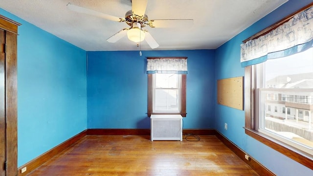 spare room with ceiling fan, radiator heating unit, light wood-style flooring, and baseboards