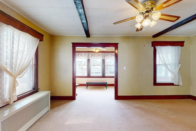 spare room with a healthy amount of sunlight, carpet flooring, beamed ceiling, and radiator heating unit