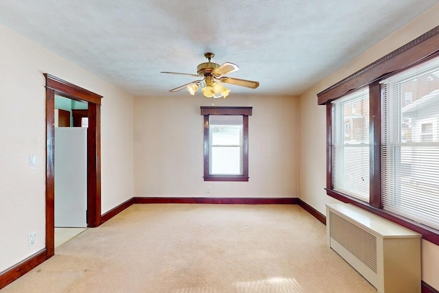 spare room featuring radiator heating unit, baseboards, ceiling fan, and light colored carpet