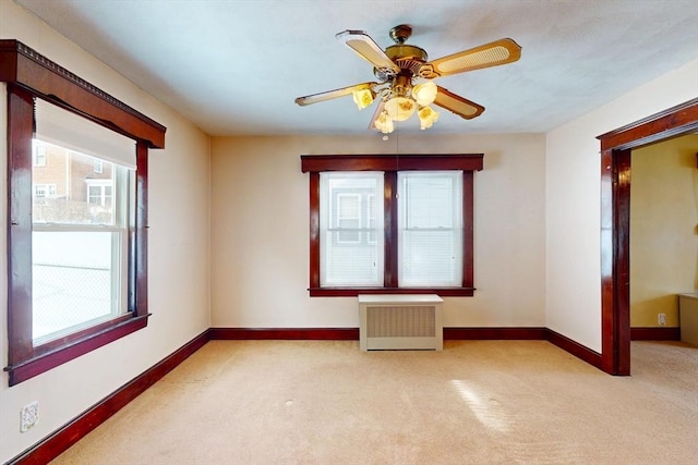 unfurnished room featuring a ceiling fan, radiator, light colored carpet, and baseboards