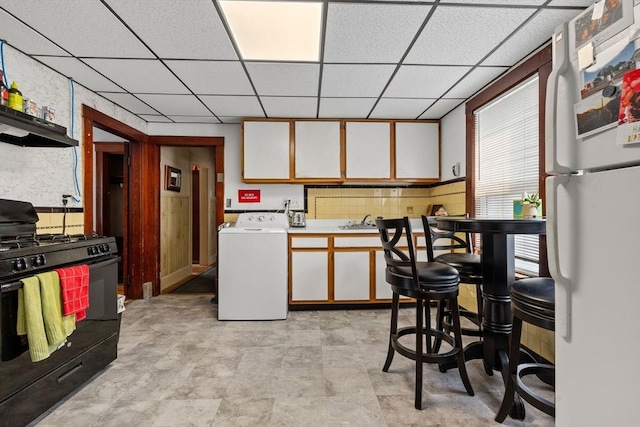 kitchen featuring black gas stove, freestanding refrigerator, washer / dryer, and a drop ceiling