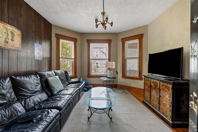living area featuring wood finished floors, wood walls, a textured ceiling, and a notable chandelier