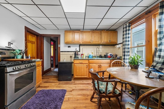 kitchen featuring decorative backsplash, light wood-style floors, a drop ceiling, stainless steel range with gas cooktop, and a sink