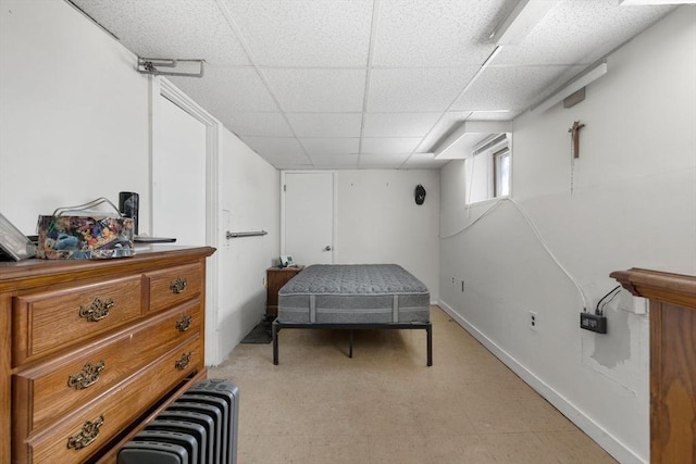 bedroom featuring a drop ceiling, radiator, and light floors
