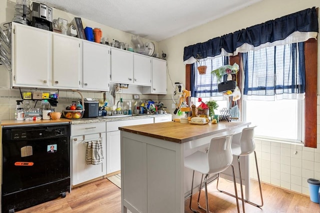 kitchen with wooden counters, dishwasher, a sink, white cabinets, and light wood-style floors