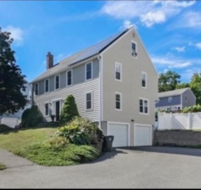 view of property exterior featuring a garage, fence, a chimney, and aphalt driveway