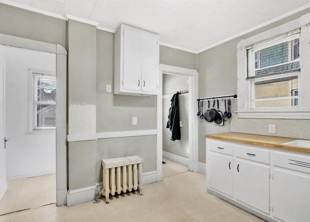 kitchen featuring baseboards, radiator heating unit, white cabinetry, and crown molding