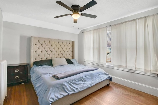 bedroom with ceiling fan, wood finished floors, baseboards, vaulted ceiling, and radiator