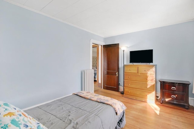 bedroom featuring baseboards, crown molding, light wood finished floors, and radiator heating unit