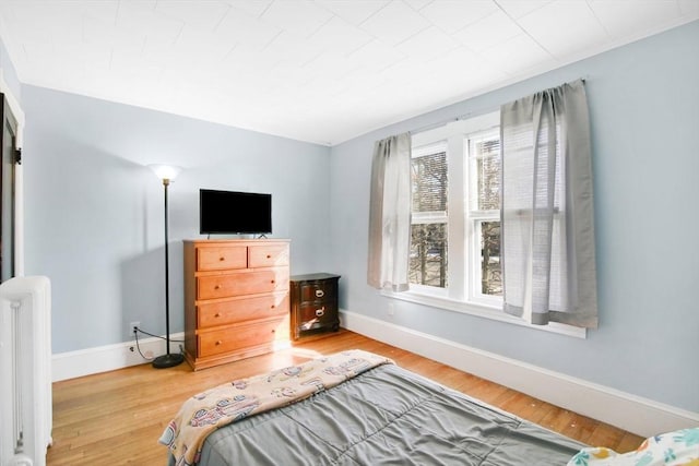 bedroom featuring radiator heating unit, baseboards, and wood finished floors