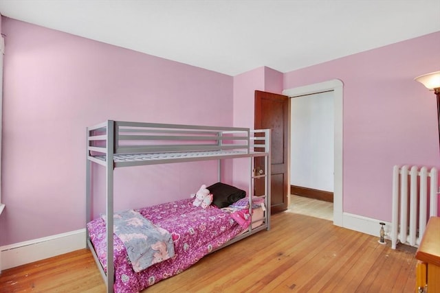 bedroom with radiator heating unit, baseboards, and wood-type flooring