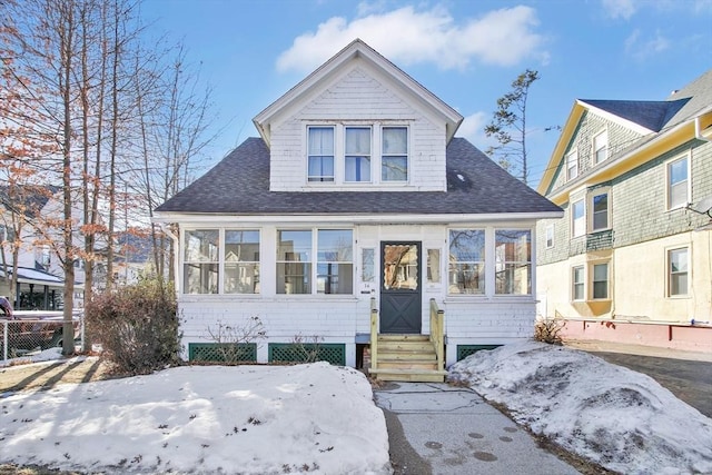 bungalow-style home with entry steps, a shingled roof, and a sunroom