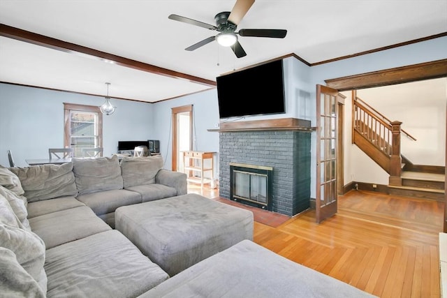 living area with a fireplace, a ceiling fan, baseboards, stairs, and crown molding