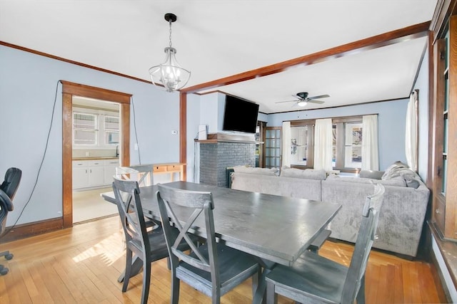 dining space featuring a brick fireplace, crown molding, light wood finished floors, and ceiling fan with notable chandelier