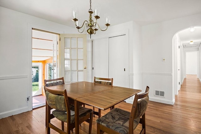 dining room featuring visible vents, light wood finished floors, a chandelier, arched walkways, and baseboards