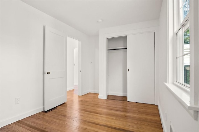 unfurnished bedroom featuring light wood finished floors, baseboards, and a closet
