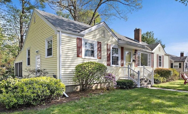 view of front facade with a shingled roof, a chimney, and a front yard