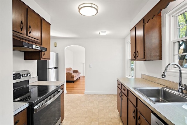 kitchen with a sink, under cabinet range hood, light countertops, arched walkways, and appliances with stainless steel finishes