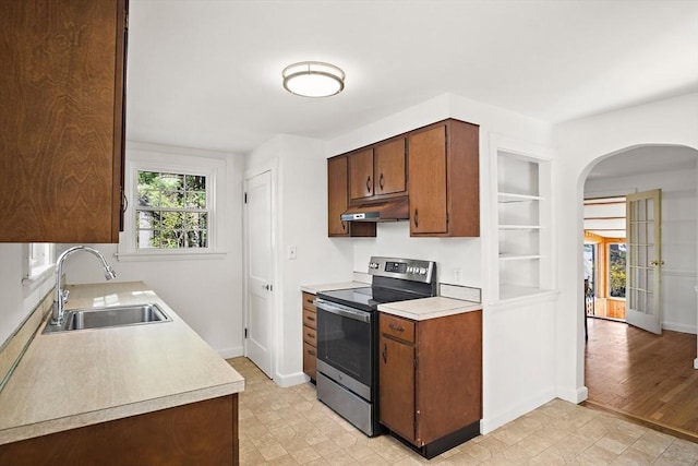 kitchen featuring a sink, arched walkways, stainless steel electric stove, under cabinet range hood, and light countertops