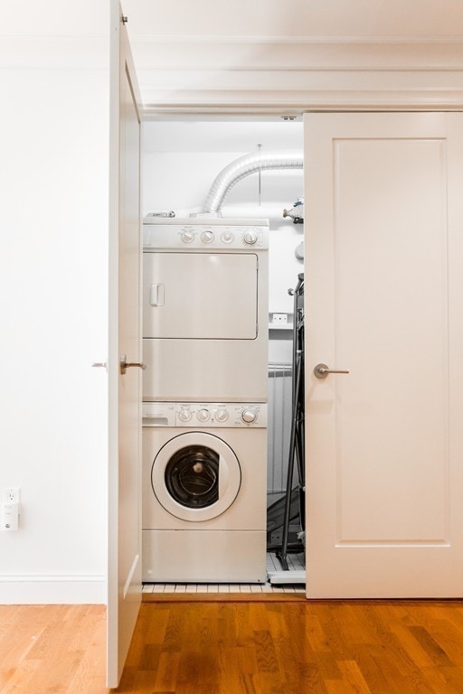 clothes washing area featuring wood-type flooring and stacked washer / drying machine