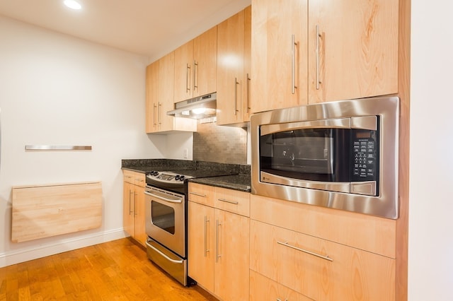 kitchen with light wood-type flooring, backsplash, dark stone counters, stainless steel appliances, and light brown cabinets