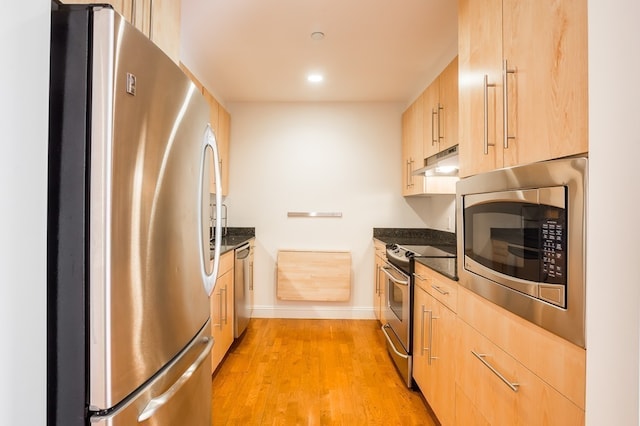 kitchen with light brown cabinetry, dark stone counters, and appliances with stainless steel finishes