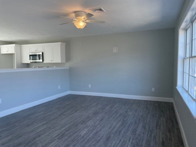 unfurnished living room featuring plenty of natural light, ceiling fan, and dark hardwood / wood-style flooring