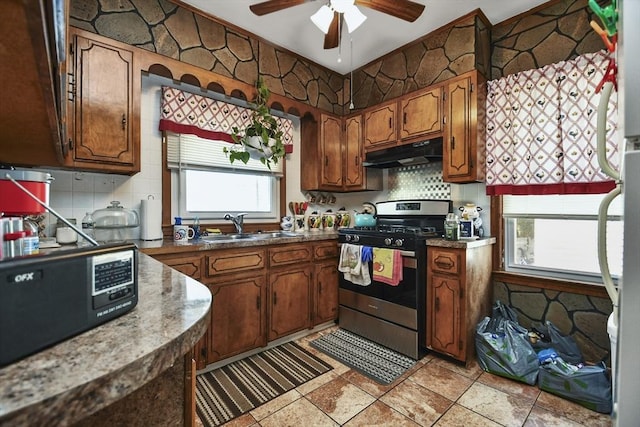 kitchen with under cabinet range hood, tasteful backsplash, stainless steel range with gas cooktop, and a sink