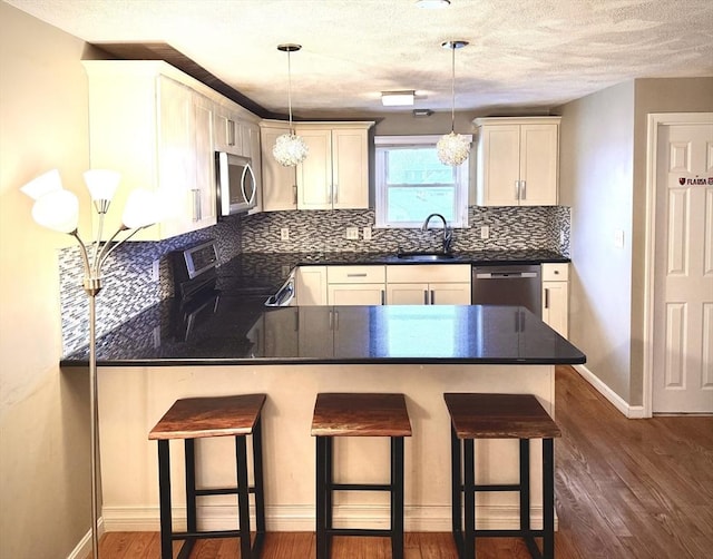 kitchen featuring tasteful backsplash, dark wood finished floors, dark countertops, appliances with stainless steel finishes, and a peninsula