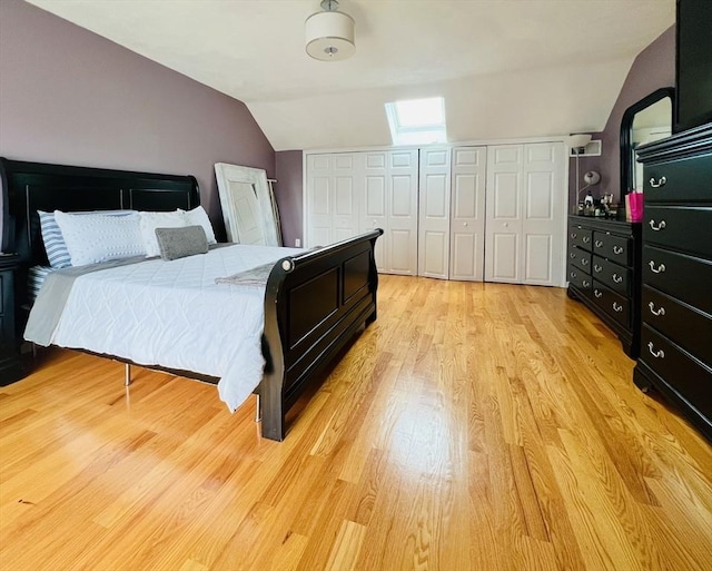 bedroom featuring vaulted ceiling with skylight, two closets, and light wood-style flooring