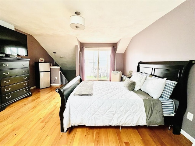 bedroom featuring baseboards, radiator heating unit, wood finished floors, freestanding refrigerator, and vaulted ceiling