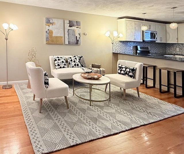 living area with a textured ceiling, light wood finished floors, and baseboards