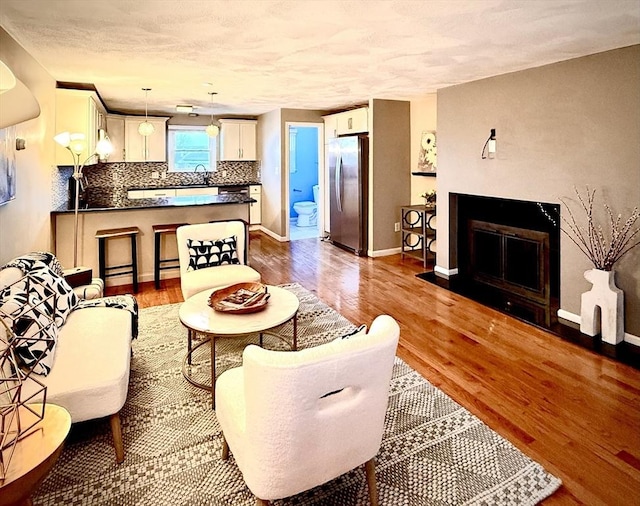 living room with a textured ceiling, wood finished floors, a fireplace with flush hearth, and baseboards