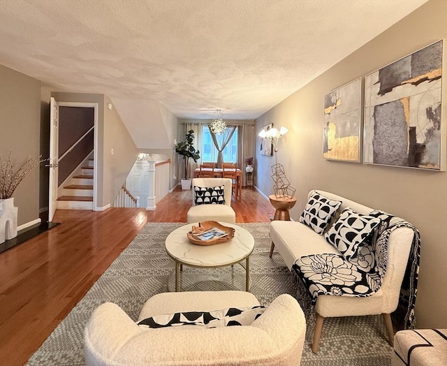 living room with stairway, a notable chandelier, a textured ceiling, and wood finished floors