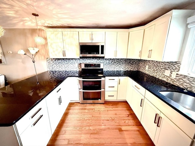 kitchen with dark countertops, backsplash, appliances with stainless steel finishes, a sink, and light wood-type flooring