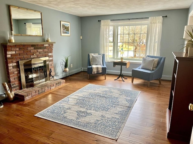 sitting room featuring a textured ceiling, a baseboard heating unit, wood finished floors, baseboards, and a brick fireplace