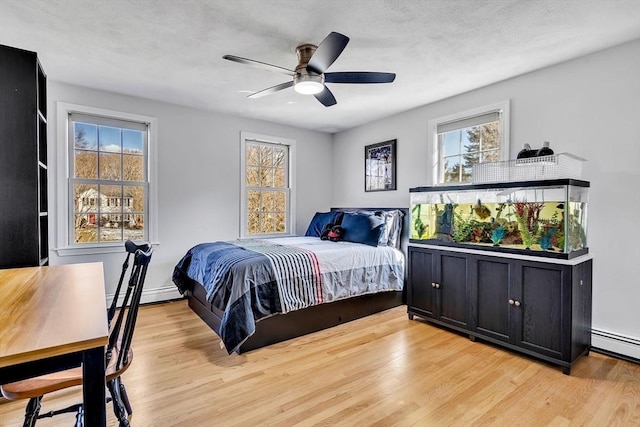 bedroom featuring baseboard heating, multiple windows, light wood-type flooring, and a ceiling fan