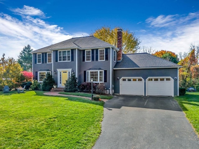 colonial-style house with a garage, a chimney, a front lawn, and aphalt driveway