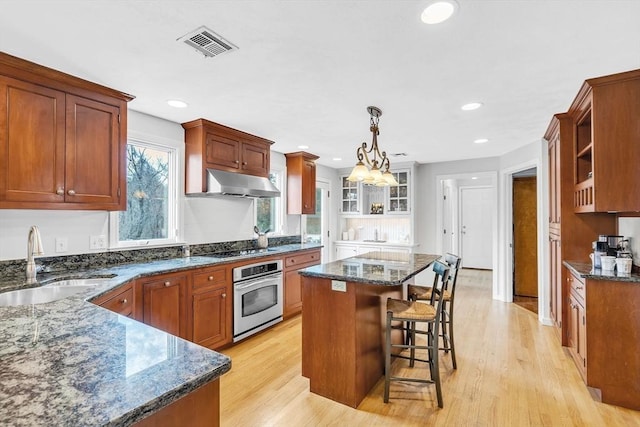 kitchen featuring visible vents, a kitchen island, under cabinet range hood, stainless steel oven, and a sink