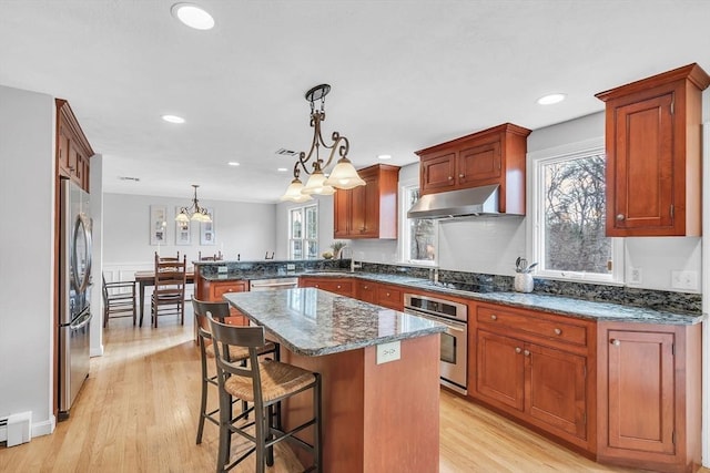 kitchen featuring light wood finished floors, a kitchen breakfast bar, a peninsula, stainless steel appliances, and under cabinet range hood