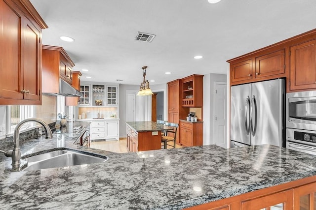 kitchen with visible vents, appliances with stainless steel finishes, glass insert cabinets, a sink, and dark stone counters