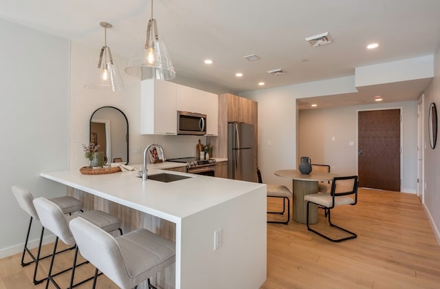 kitchen with a kitchen breakfast bar, hanging light fixtures, stainless steel appliances, and light wood-type flooring